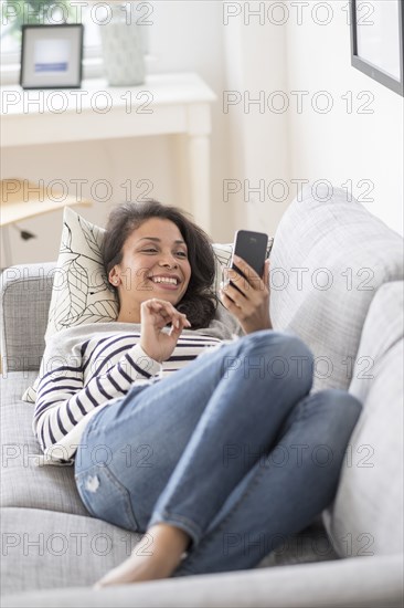 Mixed race woman using cell phone on sofa