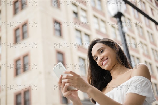 Smiling Mixed Race woman texting on cell phone in city