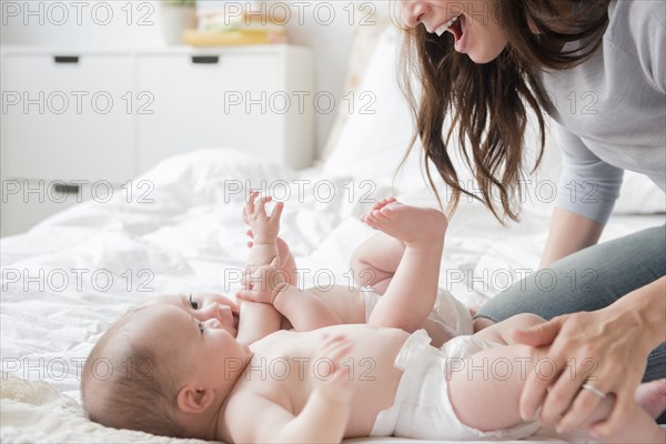 Caucasian mother playing with twin baby daughters on bed