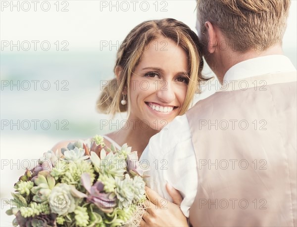 Caucasian bride and groom hugging on beach