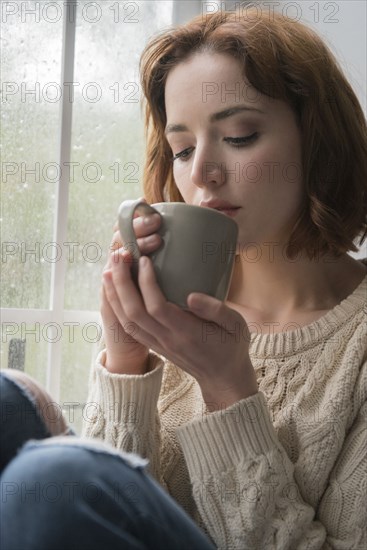 Caucasian woman drinking coffee near rainy window