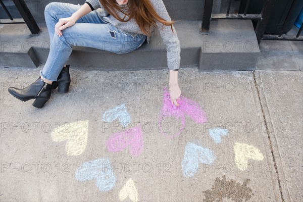 Caucasian woman drawing hearts with chalk on sidewalk