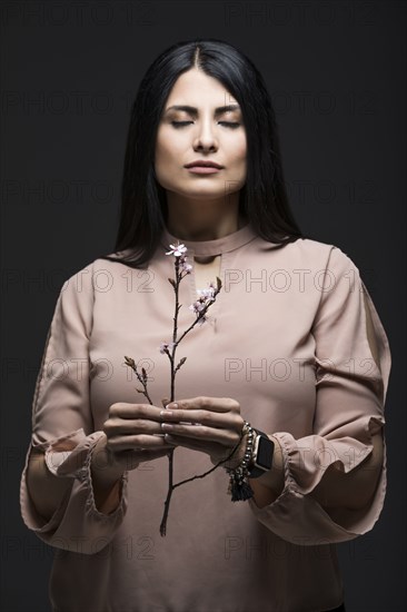 Studio portrait of woman holding blooming twig with eyes closed