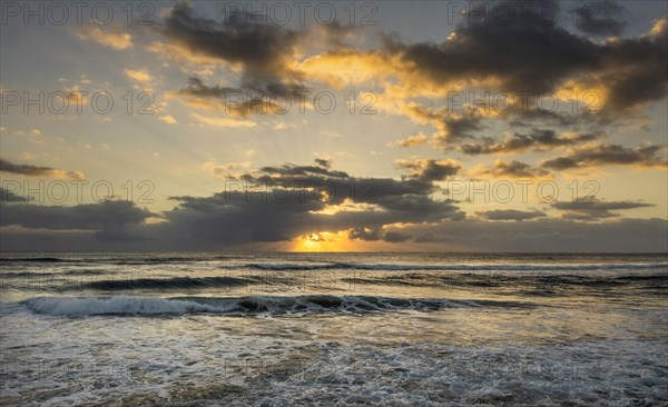 Ocean and dramatic golden streaks from morning clouds