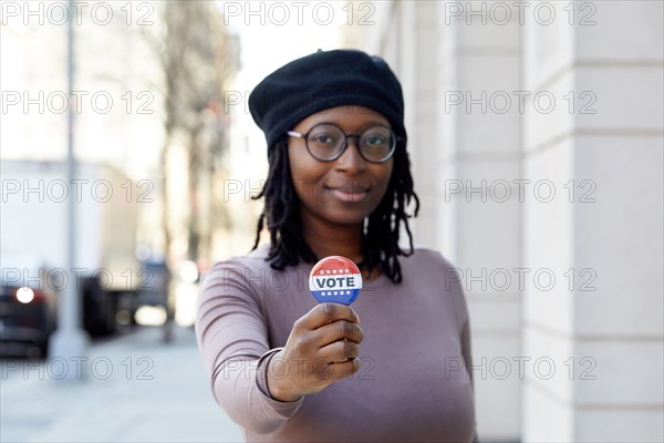 Portrait of smiling woman showing Vote button in city