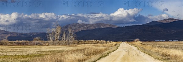 Empty dirt road leading to foothills under stormy skies