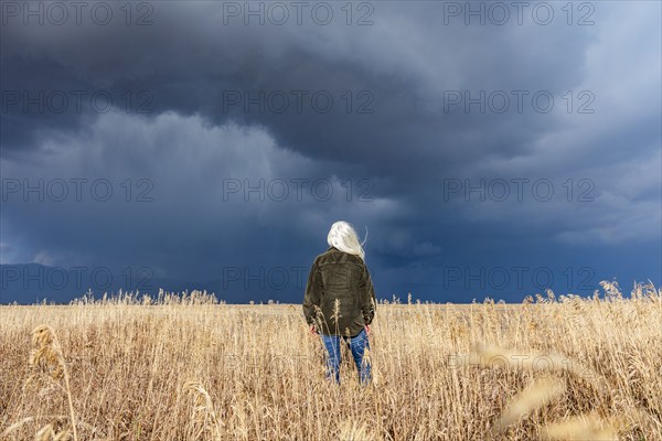 Rear view of woman standing in fall grasses under stormy sky, Fairfield, Idaho, USA