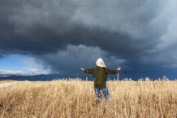 Rear view of woman standing in fall grasses under stormy sky, Fairfield, Idaho, USA