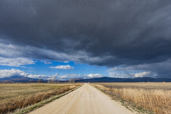 Dark storm clouds over dirt road crossing field, Fairfield, Idaho, USA