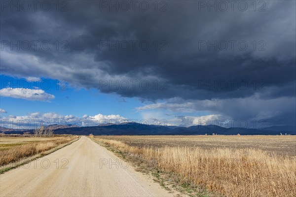 Dark storm clouds over dirt road crossing field, Fairfield, Idaho, USA