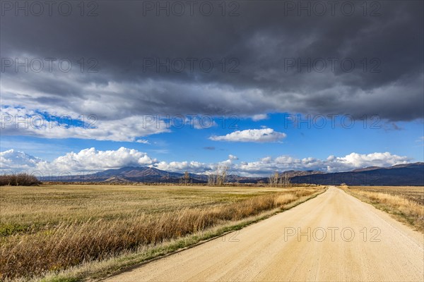 Dark storm clouds over dirt road crossing field, Fairfield, Idaho, USA