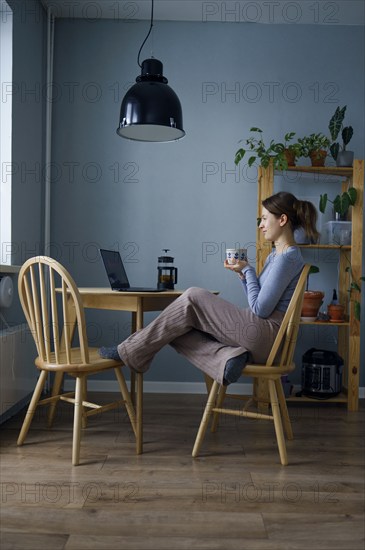 Woman holding mug and looking at laptop at home, Omsk, , Russia