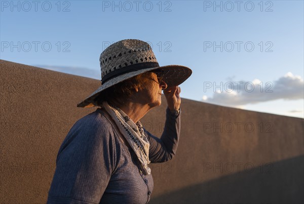 Usa, New Mexico, Santa Fe, Woman in straw hat standing against adobe wall in High Desert, Santa Fe, New Mexico, USA