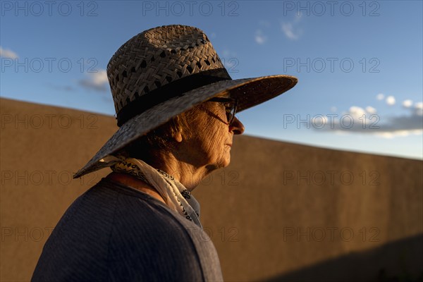 Usa, New Mexico, Santa Fe, Woman in straw hat standing against adobe wall in High Desert, Santa Fe, New Mexico, USA