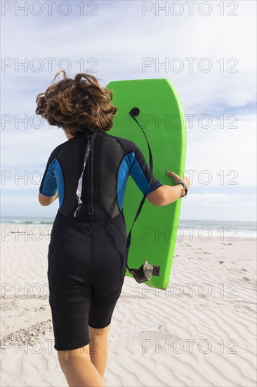 South Africa, Hermanus, Rear view of boy running on beach with body board, Hermanus, , South Africa