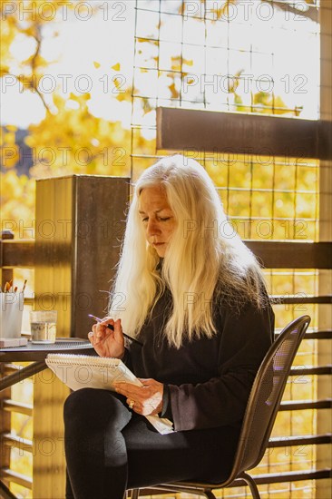 Woman with long white hair painting watercolors on deck in autumn, Springdale, Utah, USA