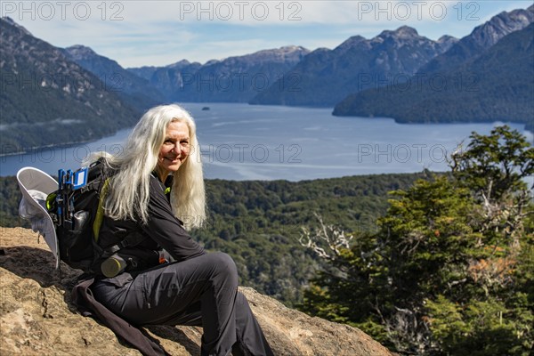 Portrait of smiling female hiker with long white hair sitting on rock above mountain lakes, Bariloche, , Argentina