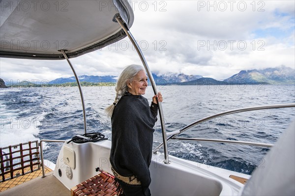 Smiling woman with long white hair standing on yacht on Lake Nahuel Huapi, Bariloche, Rio Negro, Argentina