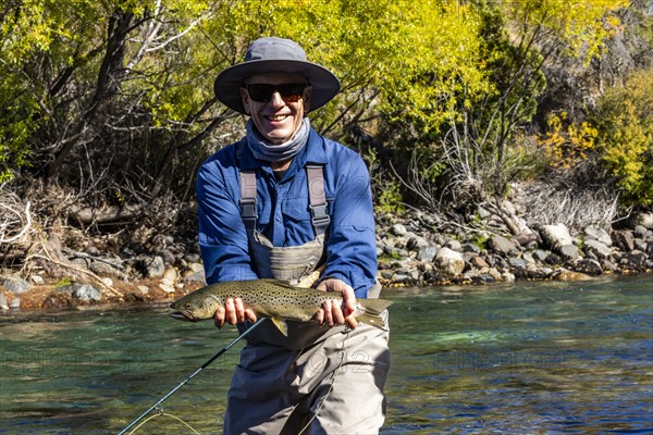 Portrait of smiling fly-fisherman holding native brown trout from Traful River before releasing it unharmed, Estancia Arroyo Verde, Nequen Province, Argentina