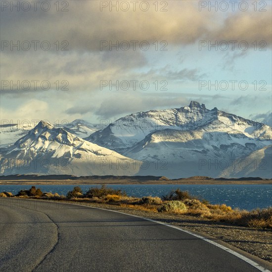 Argentina, Santa Cruz, El Calafate, Empty road with lake and snowcapped mountains in background, El Calafate, Santa Cruz, Argentina