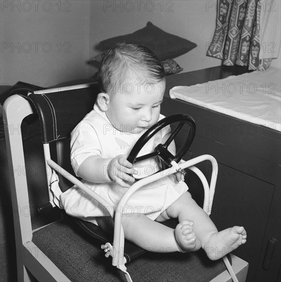 Baby at the wheel. Tubby Block's baby in a play chair with steering wheel. Kenya, 30 August 1954. Kenya, Eastern Africa, Africa.