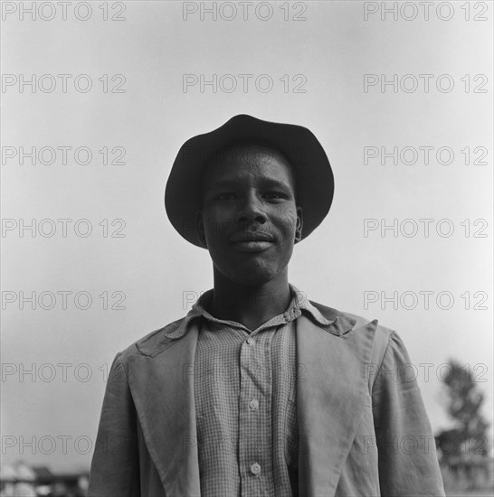 Man at a cleansing ceremony. Upper body shot of a man wearing a checked shirt, jacket and hat taken at a cleansing ceremony. Kenya, 20-28 March 1953. Kenya, Eastern Africa, Africa.