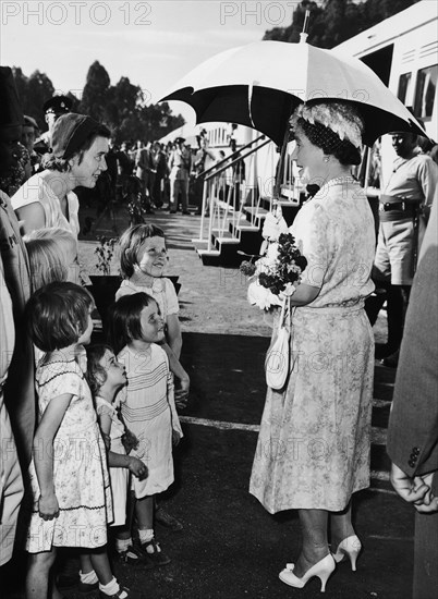 The Queen Mother visits Kenya. A publicity photograph from the East African Railways and Harbours Administration (EAR&H). Queen Elizabeth, the Queen Mother, shades herself with an umbrella as she greets a European woman and children at a stop made by the royal train on her tour of Kenya and Uganda. Central Kenya, February 1959., Central (Kenya), Kenya, Eastern Africa, Africa.