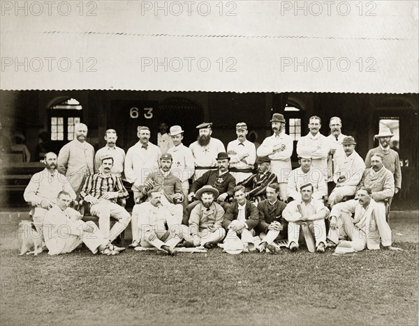 Bombay cricket teams. Players from two Bombay cricket teams line up for a group portrait outside a clubhouse. Dressed in their whites, some of the men wear padded leg guards and one holds a cricket bat. Bombay (Mumbai), India, circa 1875. Mumbai, Maharashtra, India, Southern Asia, Asia.