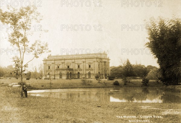 Museum in Cubbon Park. A man leans pensively against a tree in front of the museum in Cubbon Park. Bangalore, India, circa 1910. Bangalore, Karnataka, India, Southern Asia, Asia.