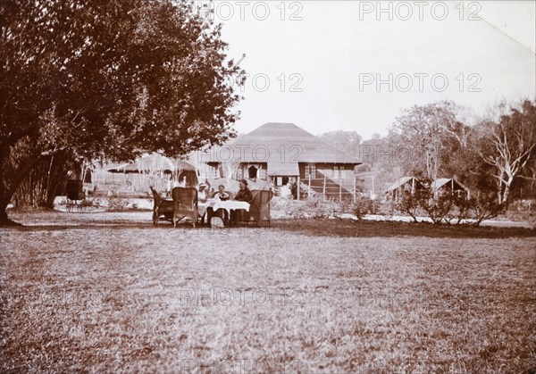 Tea party in an estate garden. Three Europeans sit at table and take tea in the garden of Mrs Browne's colonial estate. Burma (Myanmar), circa 1910. Burma (Myanmar), South East Asia, Asia.