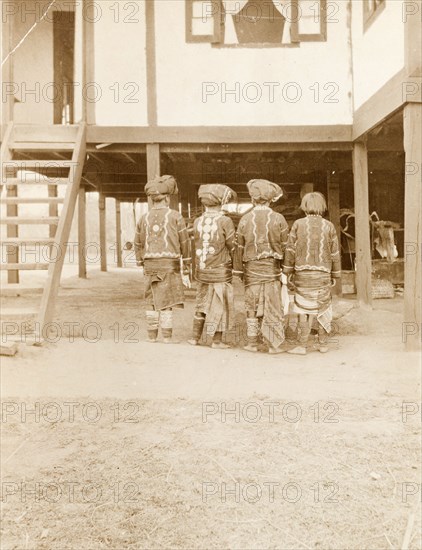 Four Kachin Women in traditional dress. Back view of four Kachin women. Dressed in traditional costume, they wear 'longyis', decorative jackets and legwear, cloth headdresses and hoops that encircle their waists. Kachin State, Burma (Myanmar), circa 1910., Kachin, Burma (Myanmar), South East Asia, Asia.