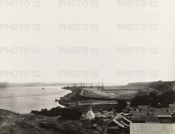 Defensive wall at the Chauk oil fields. View over the Ayeyarwady River at the Chauk oil fields, showing an access road and defence wall exposed during low water. The roofs of town buildings appear in the foreground, with a network of oil derricks in the distance. Chauk, Burma (Myanmar), circa 1931., Magway, Burma (Myanmar), South East Asia, Asia.