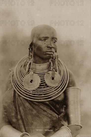 Portrait of a Maasai woman. Half-length portrait of a Maasai woman wearing numerous metal neck rings, earrings and armlets. Kenya, circa 1930. Kenya, Eastern Africa, Africa.