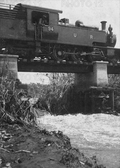 Train on washed-out bridge. A Uganda Railways locomotive pauses while crossing a damaged bridge on the Thika-Nairobi branch railway near the Fort Hall Road. Kenya, 1921., Nairobi Area, Kenya, Eastern Africa, Africa.