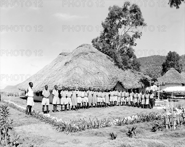 Miwani Sugar Mills school. A row of students in school uniform pose outside a thatched school hut built to educate children of workers at the Miwani Sugar Mills. A sign outside reads: 'Miwani Sugar Mills, Primary School Ltd, Section 2'. Miwani, Kenya, 7-8 November 1955. Miwani, Nyanza, Kenya, Eastern Africa, Africa.