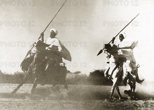 North Sudanese warriors on horseback. Two Sudanese warriors wearing white robes and turbans ride horseback, spears in hand. North Sudan, circa 1935., North (Sudan), Sudan, Eastern Africa, Africa.