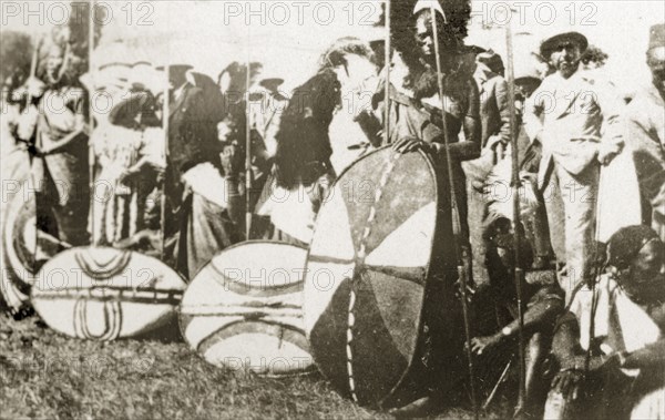 A gathering of African chiefs. A group of African chiefs dressed in ceremonial costume and headdresses, gather before European spectators holding spears and patterned shields. Nairobi, Kenya, 12-17 January 1924. Nairobi, Nairobi Area, Kenya, Eastern Africa, Africa.