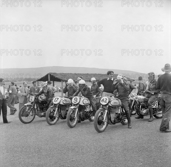 Nakuru motorcycle race. A group of riders sit astride their numbered motorcycles, adjusting their goggles at the start of a race. Nakuru, Kenya, 6 August 1956. Nakuru, Rift Valley, Kenya, Eastern Africa, Africa.