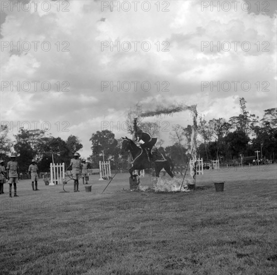 Ring of fire. A uniformed rider belonging to 67 (AT) Coy of the EAASC (East Africa Army Service Corps) demonstrates his fearless riding skills as he leaps through a ring of fire on horseback at the SJAK show (Sports Journalists Association of Kenya). Kenya, 25 August 1956. Kenya, Eastern Africa, Africa.