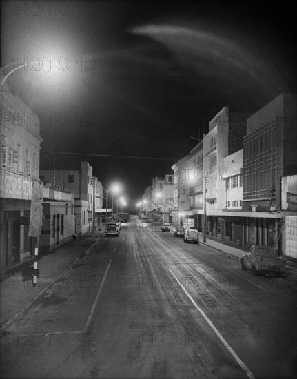 Gulzaar Street by night. Streetlights illuminate a deserted Nairobi street identified as 'Gulzaar St' lined with shops and parked cars. Nairobi, Kenya, 6 September 1956., Nairobi Area, Kenya, Eastern Africa, Africa.