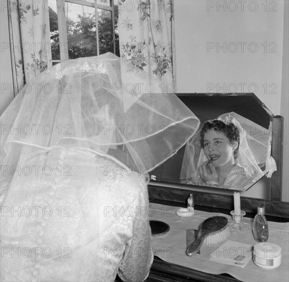 A bride at her dressing table. The Patterson bride applies her lipstick at a dressing table mirror as she prepares herself for the big day. Kenya, 29 September 1956. Kenya, Eastern Africa, Africa.