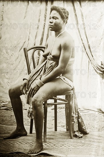 Seated woman wearing apron and beads. Studio portrait of a seated woman, wearing an under-bust apron, waistcloth and simple jewellery. Western Africa, circa 1917., Western Africa, Africa.