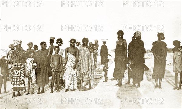 Gold Coast women and children. A group of West African women and children wearing traditional dress pose for the camera. Gold Coast (Ghana), circa 1920. Ghana, Western Africa, Africa.