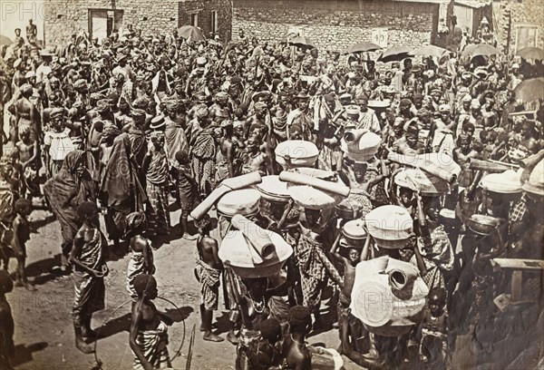 Crowds at a chief's funeral, Accra. An overhead photograph of a large mourning party gathered in the street for a deceased chief. Accra, Gold Coast (Ghana), circa 1920. Accra, East (Ghana), Ghana, Western Africa, Africa.