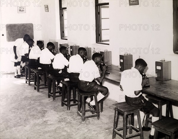 Tanganyikan students with microscopes. Official publicity shot for the Tanganyikan government. A group of young men in uniform operate microscopes during a college science lesson. Tanganyika Territory (Tanzania), circa 1950. Tanzania, Eastern Africa, Africa.