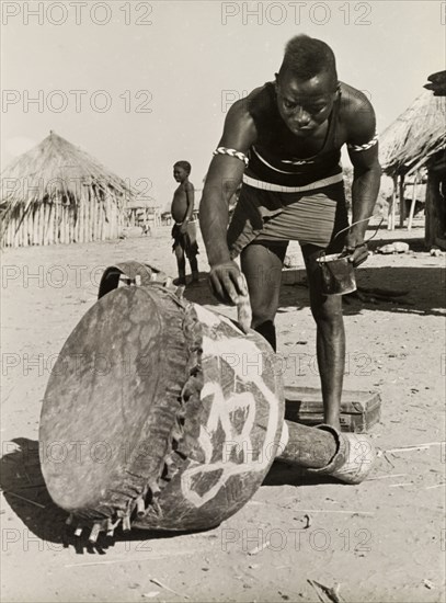 Painting a djembe drum. A Tonga (Batonga) man in traditional dress paints a decorative pattern onto a djembe drum. Probably Southern Rhodesia (Zimbabwe), circa 1955. Zimbabwe, Southern Africa, Africa.