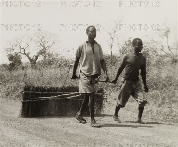 Smoothing corrugations in a road. Two men smooth over corrugations in a road by dragging a section of bound brushwood across its surface. Zomba, Nyasaland (Malawi), circa 1957., Zomba, Malawi, Southern Africa, Africa.