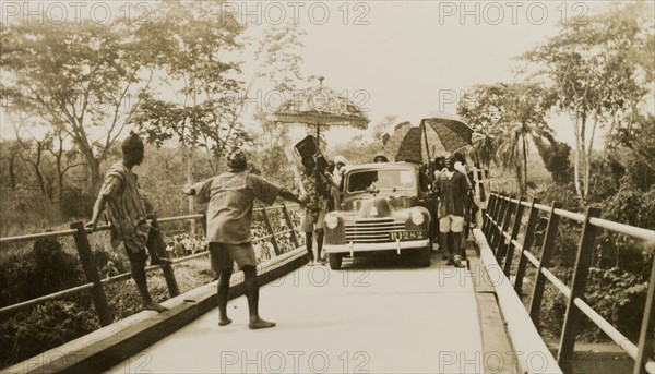 Opening of the Ishua to Ibillo bridge. People with parasols surround the first car to cross the Ishua to Ibillo road bridge at its official opening. Ondo, Nigeria, 5 January 1951., Ondo, Nigeria, Western Africa, Africa.