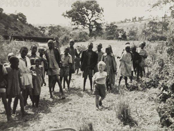 Neville Lewis plays with Kikuyu children. Neville Lewis, the eldest son of English Methodist missionary, Reverend Ian Lewis, plays amongst a group of Kikuyu children outside the Lewis family home. Limuru, Kenya, circa 1956. Limuru, Central (Kenya), Kenya, Eastern Africa, Africa.