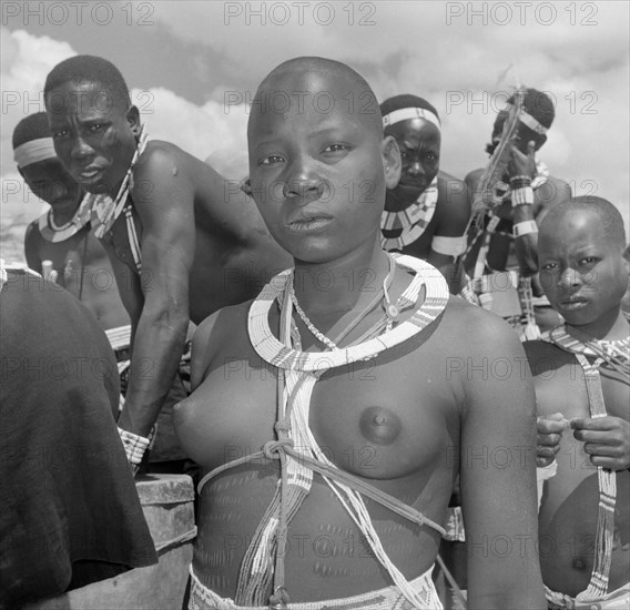 Portrait of a female Wakamba dancer. A female Wakamba dancer dressed in ceremonial costume for Princess Margaret's visit stares proudly into the camera. Naked from the waist up, she displays scarification marks on her belly, her neck and chest decorated with strings of beads. Machakos, Kenya, 22 October 1956. Machakos, East (Kenya), Kenya, Eastern Africa, Africa.